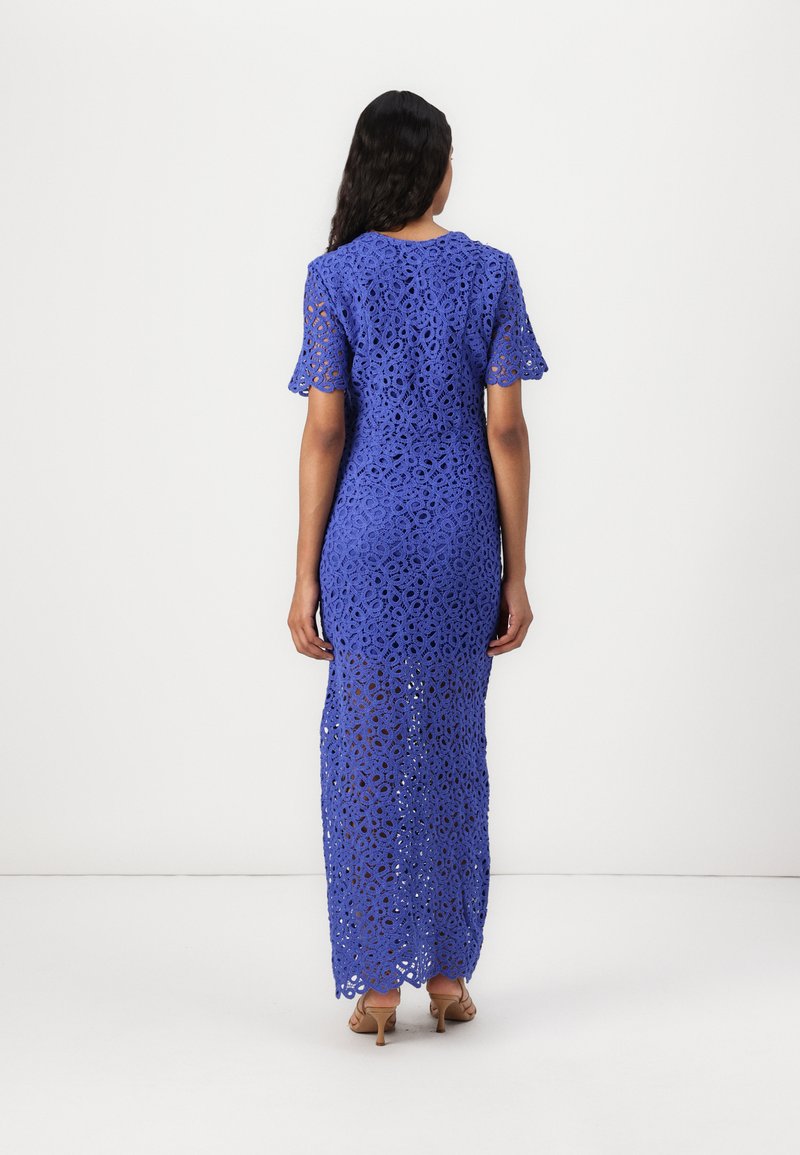Maxikleid aus blauer Spitze mit kurzen, ausgestellten Ärmeln, verziert mit filigranen Blumen-Ausschnitten und einem wellenförmigen Saum. Sanfte Textur, figurbetonte Silhouette.