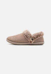 Chaussons en daim marron avec un revers en fourrure pelucheux, un bouton décoratif sur le côté et un bord cousu blanc le long de la semelle.