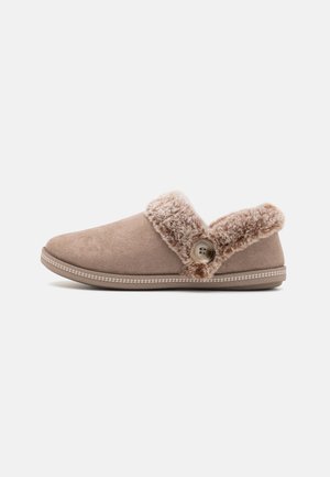 Chaussons en daim marron avec un revers en fourrure pelucheux, un bouton décoratif sur le côté et un bord cousu blanc le long de la semelle.