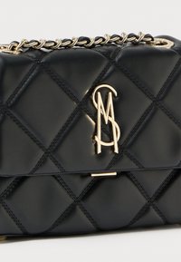 Czarna pikowana skórzana torebka z złotym łańcuszkowym paskiem, z widocznym złotym logo i detalem zamknięcia. Gładka faktura z wzorem diamentowym.