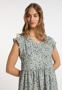 Rochie florală din țesătură bleu deschis, cu mâneci scurte volănașe, având o fustă evazată și un model de margarete mici cu accente verzi.