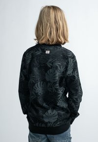 Černá mikina s texturovaným vzorem listů, s kulatým výstřihem a žebrovaným lemem, kombinována s modrými džíny.