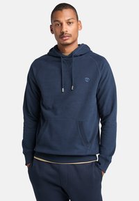 Donkerblauwe hoodie van zacht materiaal, met een zak aan de voorkant, geribbelde manchetten en een klein logo op de borst.