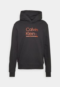 Black hooded sweatshirt with orange "Calvin Klein EST 1968" logo. Made of soft fabric, features ribbed cuffs and hem. Simple design, no patterns.