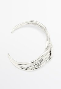 Bracciale aperto in argento con texture organica e irregolare, dall'aspetto lucido e riflettente, su sfondo bianco.