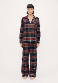 Røde og blå ternede pyjamaser med en knap-åben top og matchende bukser, med hvid piping og en brystlomme. 100% bomuldsstof, afslappet pasform.