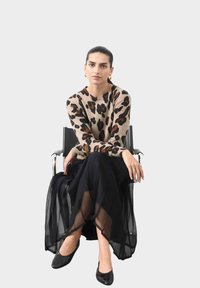 Sweter dzianinowy w brązowy leopardzi wzór na beżowym tle, zestawiony z zwiewną czarną spódnicą z tiulu. Całość dopełniają czarne płaskie buty. Srebrne kolczyki stanowią dodatkowy akcent.