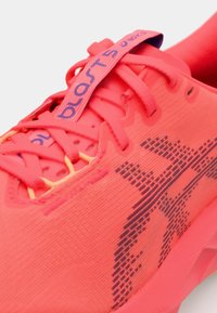 Heller pinker Sportschuh mit einem strukturierten Obermaterial aus Stoff, kontrastierenden gelben Schnürsenkeln und einem Muster, das dunkelviolette Akzente aufweist.