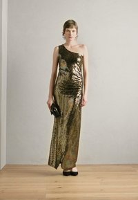 Robe de soirée dorée métallisée et noire à une épaule, avec une silhouette ajustée et une texture en sequins scintillants. Le mannequin tient une pochette noire.