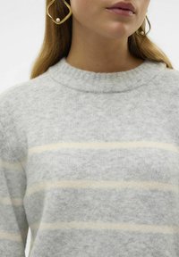 Maglione grigio a maglia con righe orizzontali crema, collo a costine, texture morbida e vista ravvicinata. Orecchini dorati con dettaglio di perla visibili.