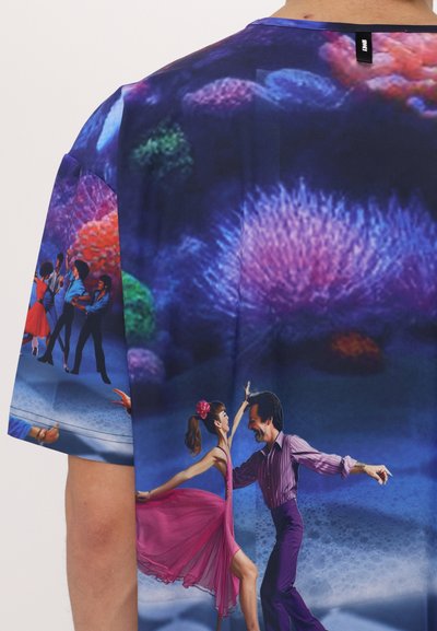 T-shirt grafico con uno sfondo vivace di barriera corallina e ballerini colorati; predominano le tonalità viola e blu, texture liscia e immagini dettagliate.