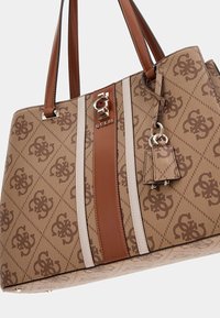 Sac fourre-tout marron et beige avec un tissu texturé, un logo décoratif, deux poignées et une étiquette d'accent. Présente des rayures verticales et des motifs subtils.