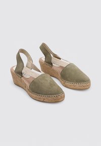 Zapatos de cuña de ante verde oliva con suela de yute natural, parte trasera abierta y una correa de tela texturizada sobre el empeine.