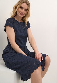 Navy lace dress with short scalloped sleeves, textured floral pattern, fitted bodice, and a flared knee-length skirt.