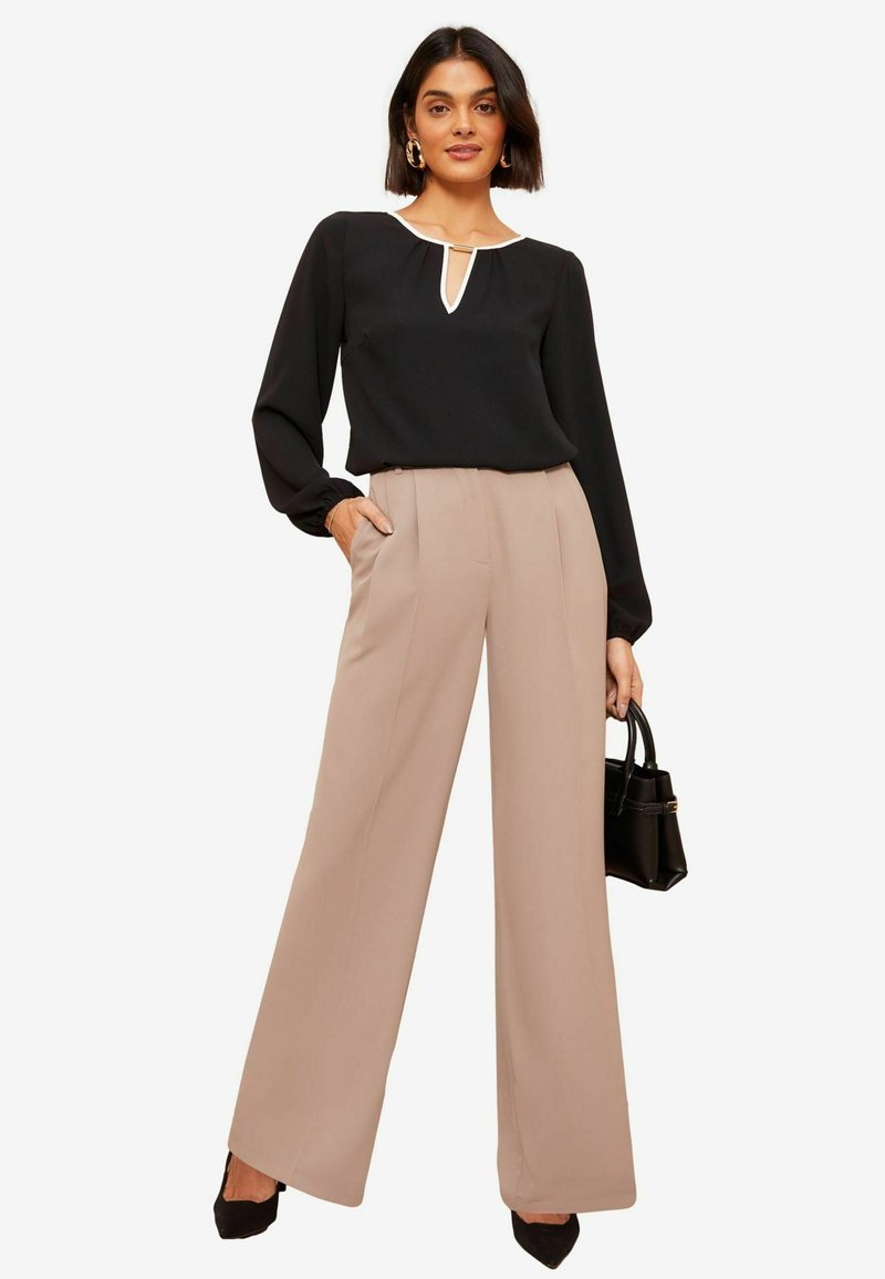 Blusa nera con dettaglio bianco sul colletto, maniche lunghe. Pantaloni larghi beige chiaro. Borsa nera e scarpe con tacco alto.