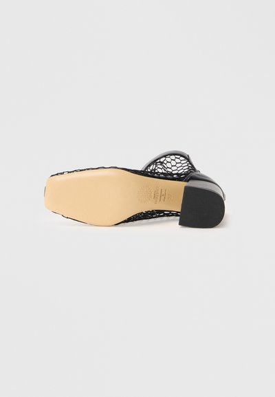 Scarpa bassa nera con tacco basso, suola beige, tomaia in rete aperta e punta quadrata, esposta con la suola rivolta verso l'alto su uno sfondo bianco.
