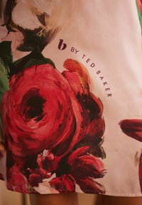 Gėlėta suknelė su didelėmis raudonomis rožėmis švelnios rožinės spalvos fone. Su prekės ženklu "b BY TED BAKER" tamsiai purpurine spalva. Lygi medžiaga.