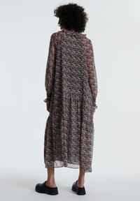 Langes, blumengemustertes Kleid aus transparenter Stoff mit Rüschensaum, langen Ärmeln und gestuftem Rock. Getragen mit schwarzen Plateauschuhen.