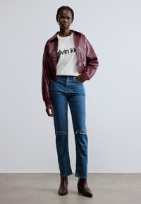 Bordo värvi lühike nahktagi valge kampsuni peal, millel must tekst, kombineerituna siniste kõrge vöökohaga teksadega, mille põlvedel on rebendid, ja pruunide kontsakingadega.