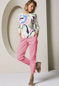 Meer-kleurige trui met abstracte patronen in pasteltinten, gecombineerd met roze broek en aangevuld met beige sleehakken.