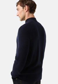 Námořnický svetřík z žebrovaného úpletu s vysokým límcem, s texturovanými rukávy a hladkým střihem těla, v kombinaci s tmavými džínami.