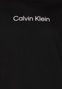 Črna bombažna majica s kratkimi rokavi, na kateri je belo napisan logotip "Calvin Klein" čez prsa, s krožnim izrezom.