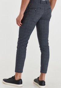 Pantalon slim en flanelle à carreaux bleu marine avec poches arrière, porté avec des baskets noires, vu de la taille vers le bas et légèrement tourné sur le côté.