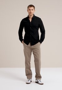 Cămașă neagră cu mâneci lungi și deschidere cu nasturi, asortată cu pantaloni bej și adidași albi cu dungi negre. Design simplu, croit.