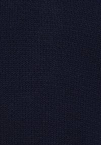 Tummansininen neulottu kangas tiheällä, tasaisella ommellekuviolla ja näkyvällä tekstuurilla.