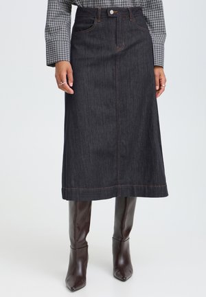 Jupe midi en denim foncé avec poches avant et fermeture par boutons, portée avec une chemise à carreaux à manches longues et des bottes marron à bout pointu.