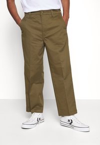 Khaki kalhoty se přímým střihem, s knoflíkovým zapínáním a bočními kapsami, v kombinaci s bílými nízkými teniskami. Hladký bavlněný materiál.