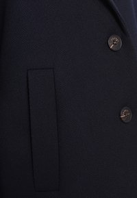 Gros plan sur un tissu texturé foncé avec une poche verticale et deux boutons ronds noirs étiquetés "Esprit."