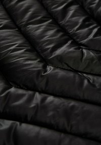 Tejido acolchado negro con textura suave, presentando patrones de costura diagonal y un acabado brillante. Apariencia suave y esponjosa.