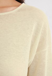 Maglione a maglia giallo chiaro con una texture morbida. Presenta un collo rotondo e una vestibilità ampia, mettendo in risalto un aspetto leggermente trasparente.