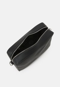 Borse in pelle nera con un design bicolore, dotata di una cerniera argentata e una tirazip a forma di anello. Texture liscia con una forma strutturata.