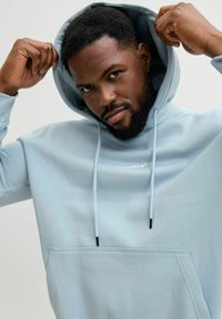 Sweat à capuche bleu clair en tissu doux, avec une poche avant, des cordons de serrage et un petit logo sur la poitrine.