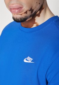 Blå bomuld T-shirt med rund halsudskæring og korte ærmer, med hvid Nike-logo på brystet og synlig tekstur.