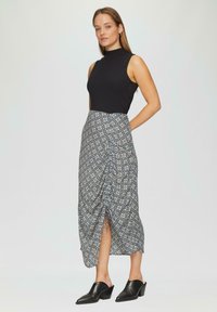 Haut noir à fines côtes sans manches associé à une jupe maxi à motifs en bleu, crème et beige. La jupe présente une fente latérale et des détails froncés.