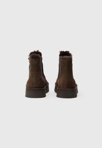 Bruine suède enkellaarsjes met een gestructureerde schacht, een bontvoering bij de kraag en een ronde neus. Voorzien van een stevige, vlakke rubberen zool.