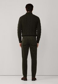 Pull en tricot côtelé vert foncé avec un col montant, associé à un pantalon olive slim-fit et des chaussures marron, vu de dos.