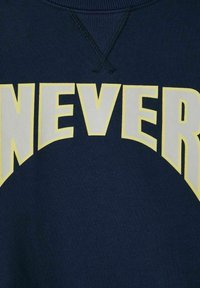 Felpa navy con testo giallo in evidenza che legge "NEVER" in lettere grasse e testurizzate sul petto. Design classico con colletto a girocollo.