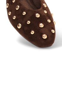 Zapato de ante marrón con punta afilada, adornado con tachuelas doradas dispuestas uniformemente por toda la superficie. Textura suave con un diseño minimalista.