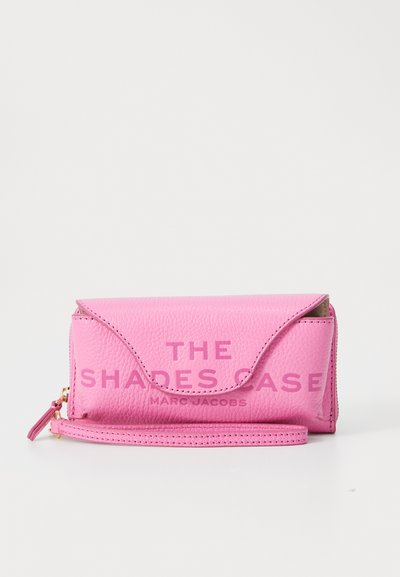 Rozā ādas saulesbrillēm paredzēta korpusa ar teksturētu virsmu, kurā ir iepresēts teksts "THE SHADES CASE" un "MARC JACOBS." Ar rāvējslēdzēja aizdari.