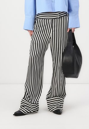 Pantalons rayés noir et blanc avec une coupe évasée, dotés d'un ourlet à revers. Associés à une chemise bleu clair et un sac à main noir.