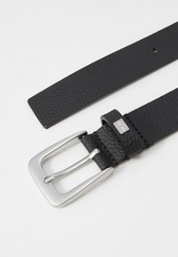 Ceinture en cuir noir avec une finition texturée, dotée d'une boucle en métal argenté et d'un accent de marque près de la boucle.