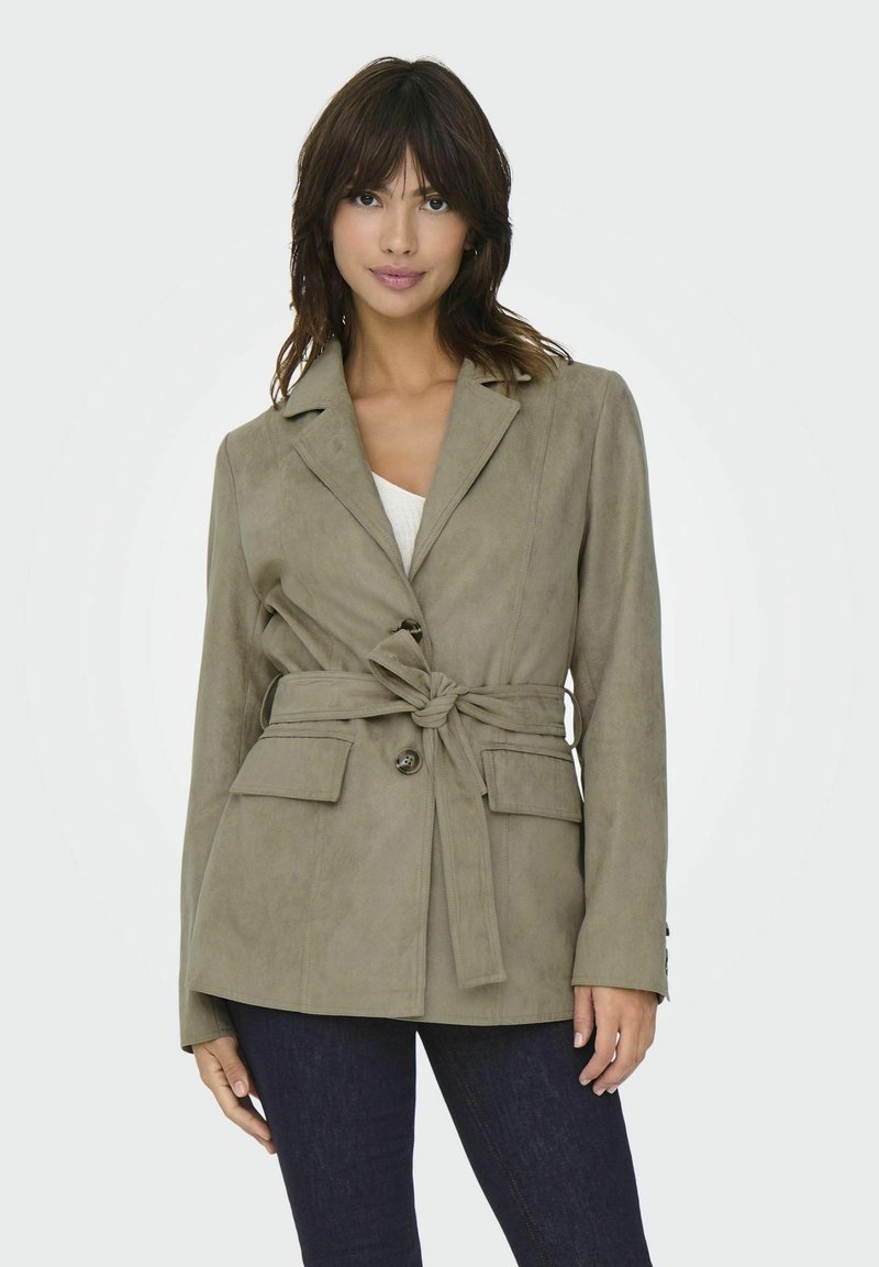 Beige, faux-suède blazer met een strikceintuur, notch revers, twee voorzakken en knoopdetails. Harlow textuur en gestructureerd ontwerp.