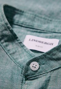 Groene linnen shirt met een button-down kraag, een enkele knop bij de hals en een label met de tekst "Lindbergh Slim Fit."