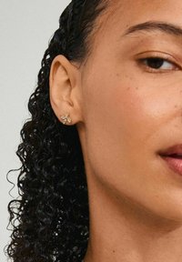 Ušne naušnice zlatnog tona u obliku zmaja muha, s naglascima od prozirnih dragulja. Close-up pogled koji ističe ušno resicu i teksturu naušnica.