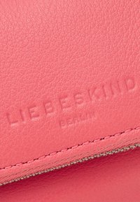Superficie in pelle testurizzata rosa con logo in rilievo "LIEBESKIND BERLIN" sopra una cerniera argentata e una cucitura.