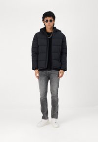 Zwarte donsjack met een capuchon, met een gestikt ontwerp. Draag het over een zwarte top, gecombineerd met grijze jeans en witte sneakers. Ronde zonnebril.